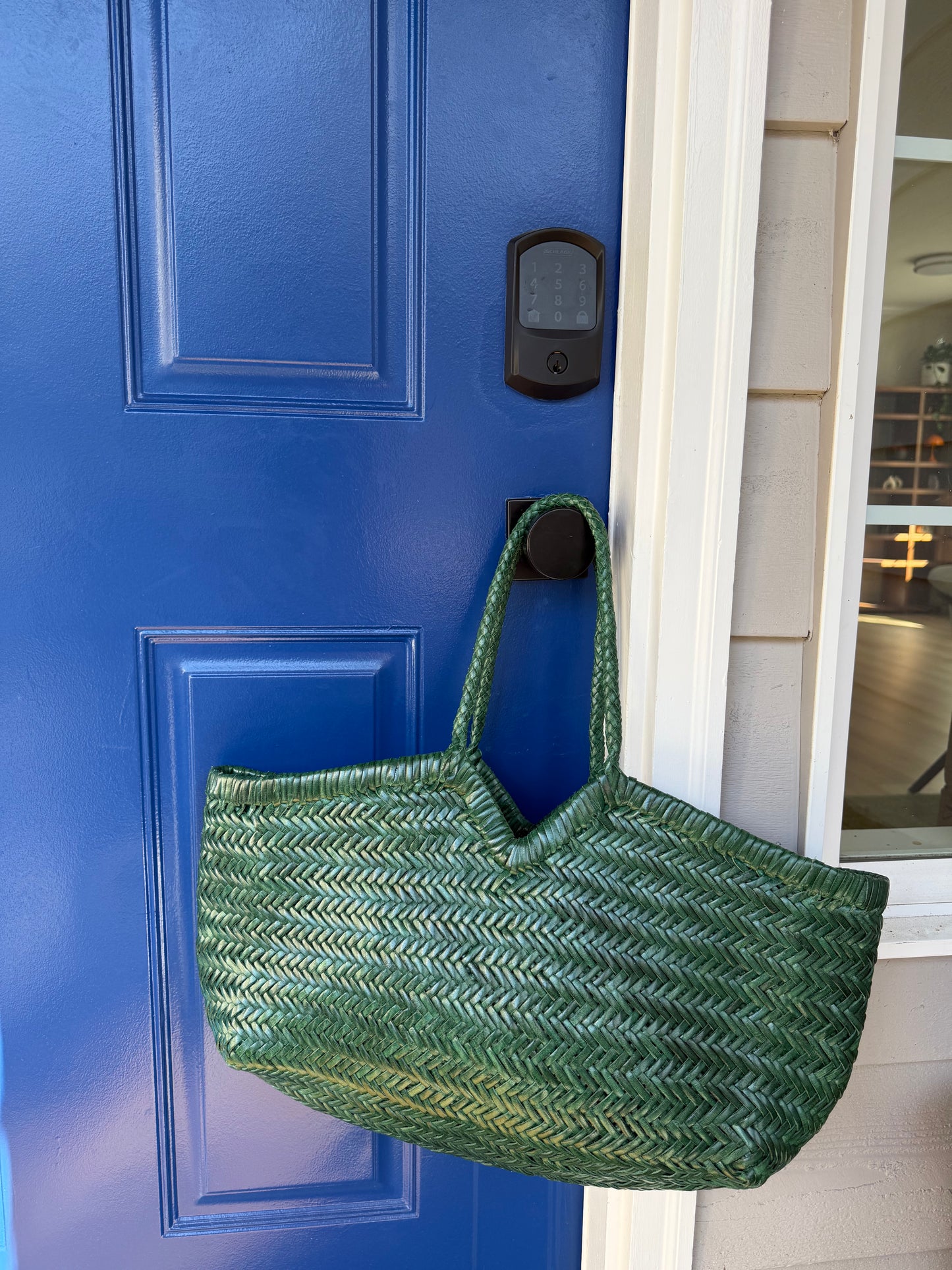 ELETTA woven leather shoulder bag styled against a blue door