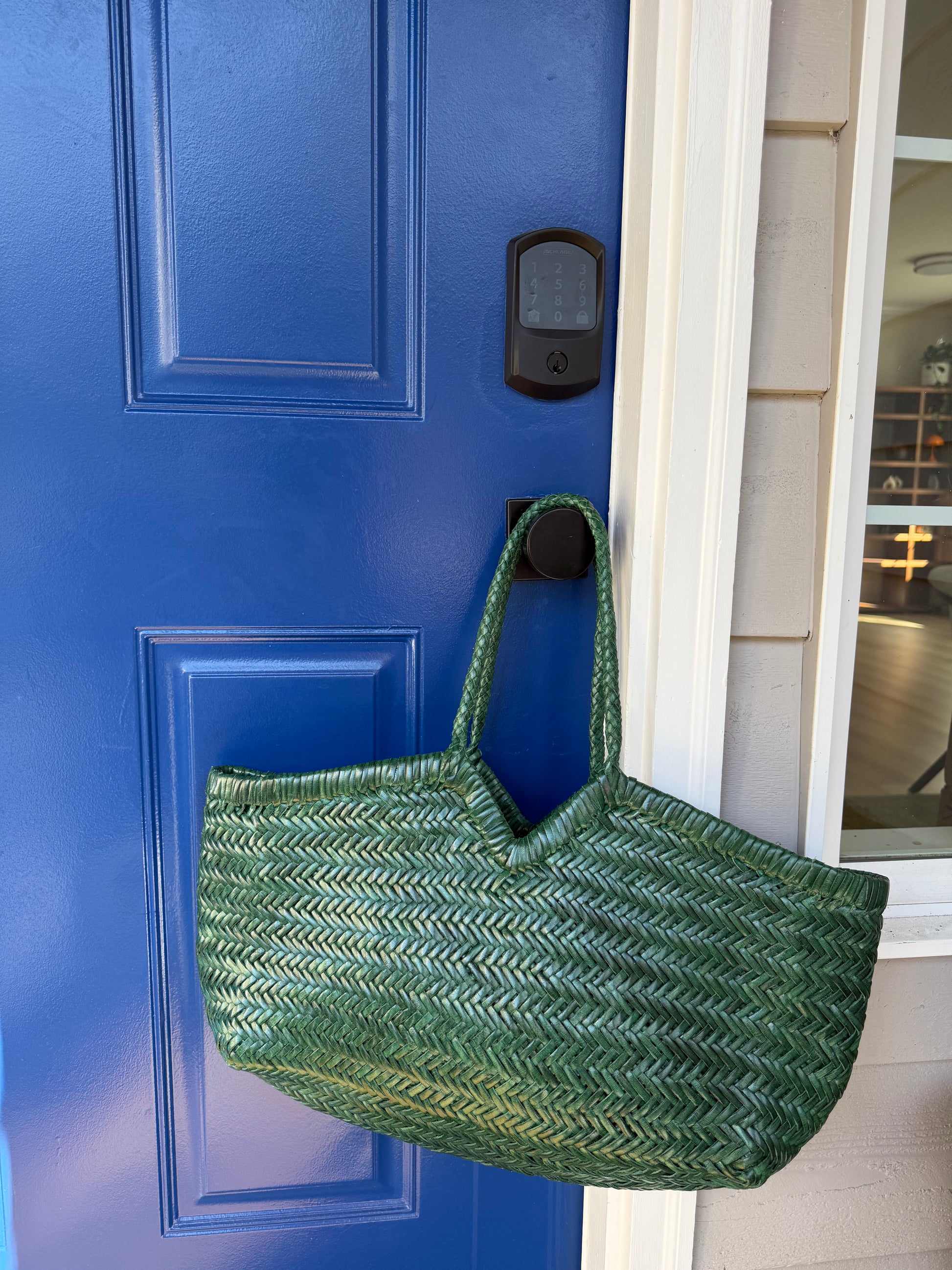 ELETTA woven leather shoulder bag styled against a blue door